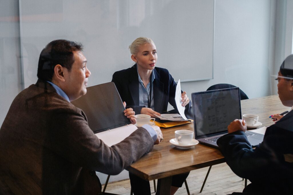 pexels-photo-5668492-5668492 Multiracial colleagues in formal clothes sitting at table with laptop and documents while discussing details of business plan